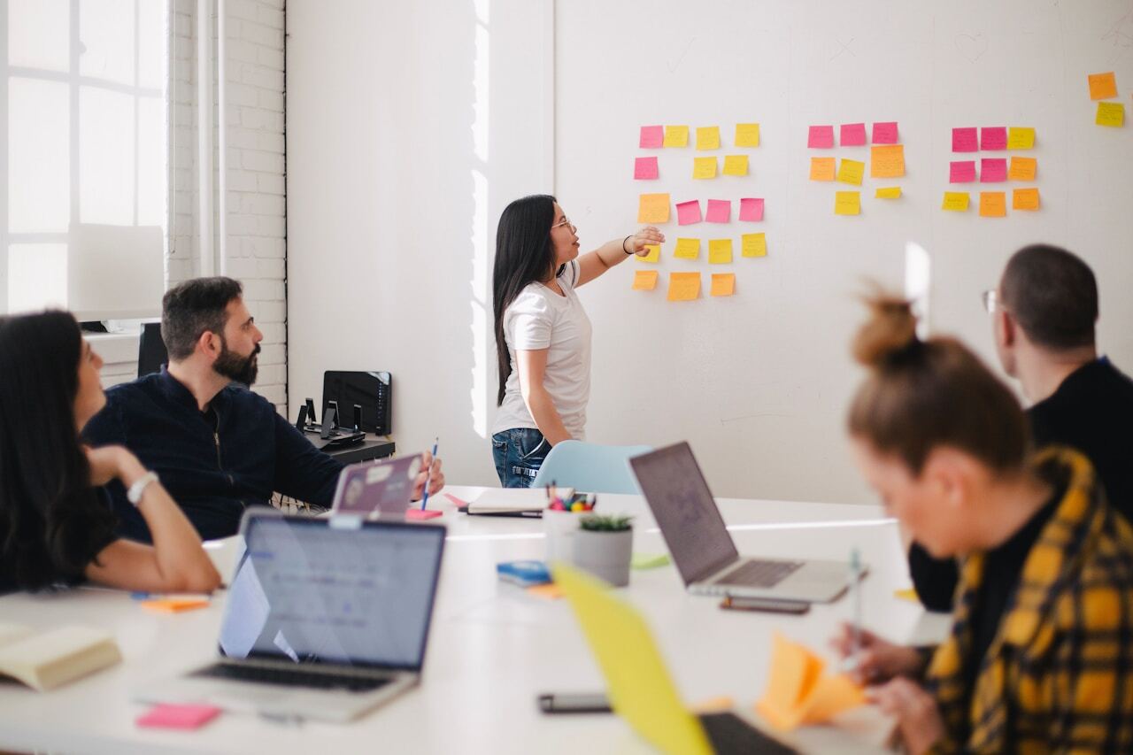 Team using sticky notes on a whiteboard in a meeting room with laptop computers on a table
